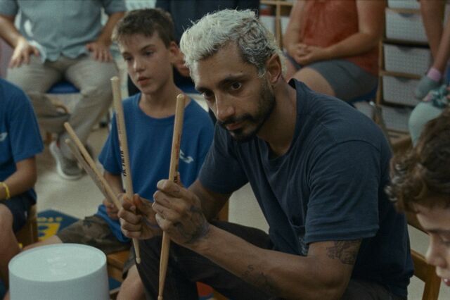 Drummer Ruben zit in het midden van een groep kinderen. Hij toont hen hoe ze hun drumstokken moeten vasthouden.