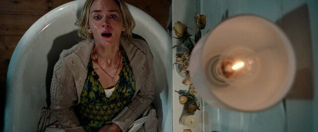 Still uit de film A Quiet Place. Evelyn zit aangekleed in een leeg bad. Ze kijkt angstig omhoog